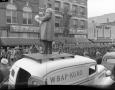 Photograph: [Soldiers pass reporter standing on a vehicle]