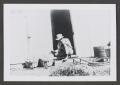 Primary view of [Photograph of a man sitting in a doorway next to baskets of produce]