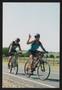 Photograph: [Two cyclists riding and waving: Lone Star Ride 2002 event photo]