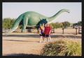 Photograph: [Two women posed in front of a large green dinosaur statue: Lone Star…
