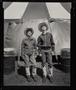 Photograph: [Two boys in western attire, standing in front of a circus tent]