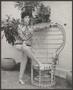 Primary view of [Woman posing next to a rattan peacock chair]