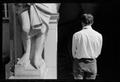 Photograph: [Man standing at the feet of a statue]