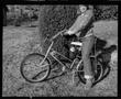 Photograph: [Child on a bicycle in front of a bush]