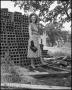 Photograph: [Woman stands next to a pile of bricks]