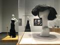 Primary view of [A hat by Cristobal Balenciaga in front of evening dresses]