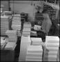 Photograph: [Bookbinder seated at desk putting paste on books]