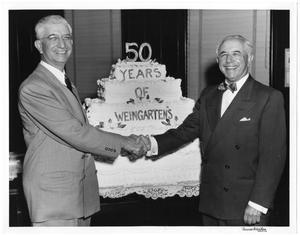 [Abe and Joe Weingarten shaking hands in front of 50 years of Weingarten's cake]