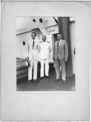 [Three unidentified men, one dressed as naval officer in front of doorway]