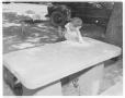 Photograph: [A boy leaning on a memorial table at Camp Ben McCullouch]