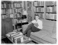 Photograph: [Richard Yarborough sitting on a couch reading a book]
