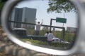 Primary view of [The side mirror of a police car reflects a man standing in the back of a pick-up truck]