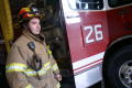 Primary view of [A fireman smiles as he stands beside his fire truck in his fire-fighting gear]