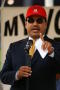 Photograph: [Close-up of Luis de la Garza speaking at microphone wearing red hat]