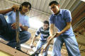 Photograph: [Three students work on the roof of a structure they are building]