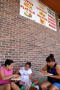 Primary view of [Two women and young girl eating while sitting next to brick wall]