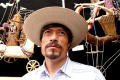 Primary view of [Man in straw hat gazing upward with craft items hanging in background]