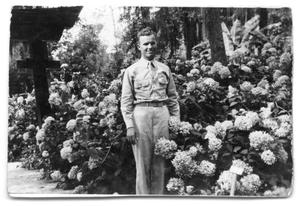Primary view of object titled '[Buddy Sinclair in uniform by flower bush]'.