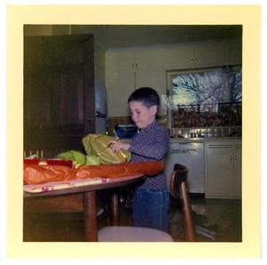 Primary view of object titled 'Boy at a table opening a package'.