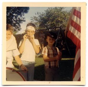 Primary view of object titled 'Three boys in a back yard during a Fourth of July parade'.