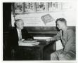 Photograph: Two Men Speaking at a Desk