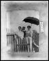 Photograph: Three Women Under Umbrella by Fence