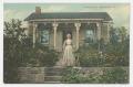 Primary view of [Postcard of an Older Woman Standing in Front of a House]