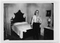 Photograph: [Otto Lindig Holding a Photo and Standing at the Foot of a Bed]