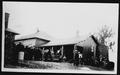 Primary view of [Large group of men standing around the porch of the cabin at Camp George]