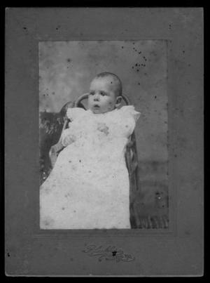 Primary view of object titled '[An infant sitting in a chair and wearing a white gown with lace insets]'.