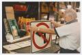 Photograph: [Man inspecting No-Left-Turn sign in shop]