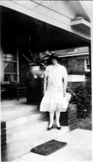 Primary view of object titled '[Aline standing on steps, wearing a white lace dress and a black hat]'.