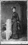 Primary view of [A woman standing beside a chair wearing a black dress and hat]