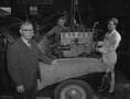 Photograph: [Three Men Standing Around a Car as the Engine Is Lowered]