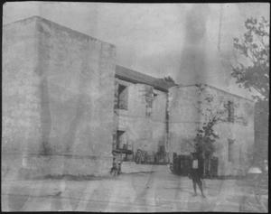 Primary view of object titled '[A young boy standing outside of a two story stucco building]'.