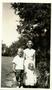 Photograph: [Barbara McCampbell standing in a yard with a young boy and a young g…