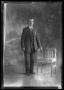 Photograph: [Portrait of Man Standing Beside Chair]