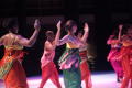Photograph: [Ensemble in colorful costumes with arms up]