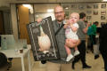 Photograph: [Man Holding Poster In One Hand and Baby In Other]