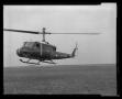 Photograph: [Photograph of a UH-1F Iroquois helicopter above a field]