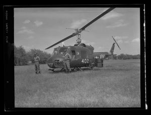 Primary view of object titled '[Photograph of two soldiers standing by a UH-1B Iroquois helicopter in a field]'.