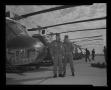 Photograph: [Photograph of two men posing in front of a row of UH-1F Iroquois hel…