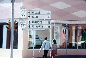 Primary view of object titled '[Two people walking under Texas road signs]'.