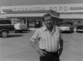 Photograph: [Man standing in front of a Ford dealership, 4]