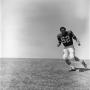 Photograph: [Football player #52 Jerry Robinson jogging down a grass incline from…