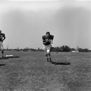 Primary view of object titled '[Football player #74 jogging center frame and #62, Bob Tricks, standing to the side]'.