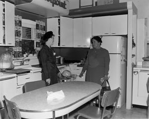 Primary view of object titled '[Two women stand on Hotpoint kitchen set]'.