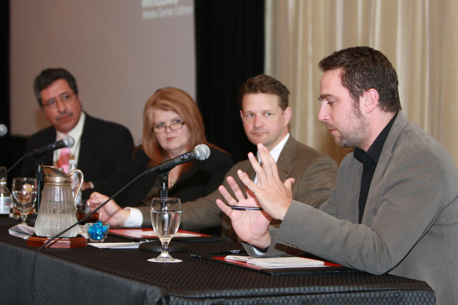 [Guest panelists at TDNA conference], Photograph of unidentified guest panelist attending the 2010 Texas Daily Newspaper Association annual meeting held in Houston, Texas. The man in the foreground is seen talking into the microphone, using his hands as emphasis as he speaks, while his guest panelists watch him., 