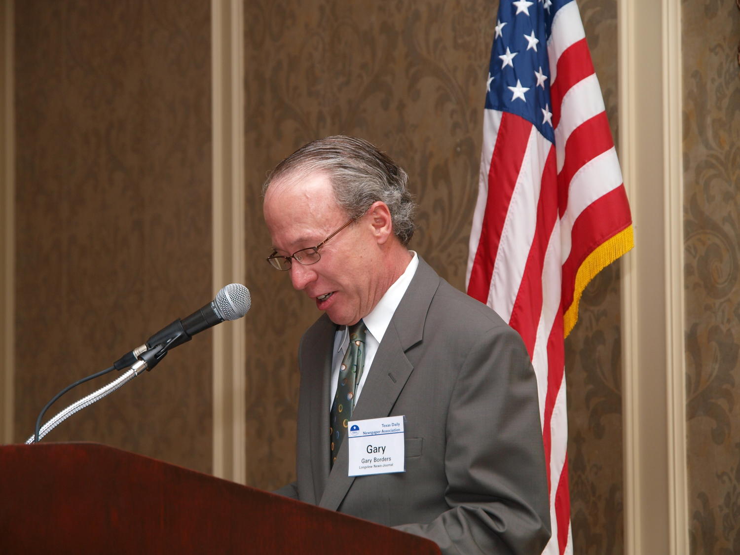 [Gary Borders speaking into mic during TDNA award ceremony], Photograph of Gary Borders standing at a podium and speaking into the microphone during the award ceremony at the 2008 Texas Daily Newspaper Association annual conference awards dinner, held at The Westin Riverwalk Hotel in San Antonio, Texas., 