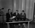 Photograph: [Three men seated at table with microphone]